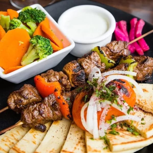 Kabob House's beef shish kabobs with vegetables, pita bread, pickled turnips, and a white dipping sauce.