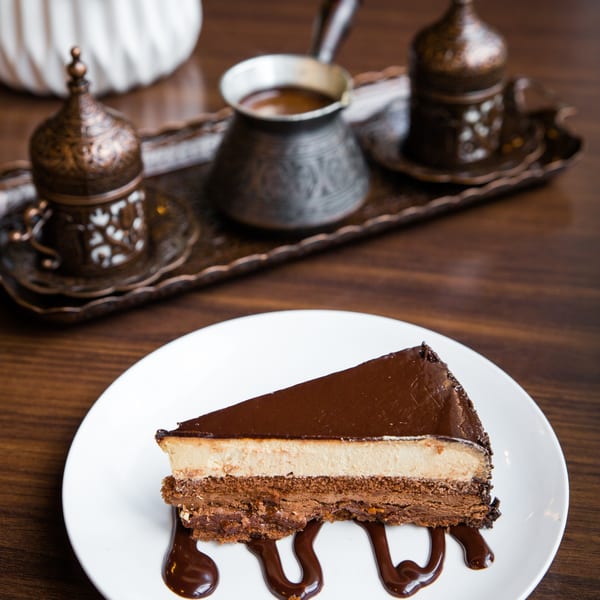 A slice of chocolate cake with a creamy filling and chocolate drizzle, served with Turkish coffee.