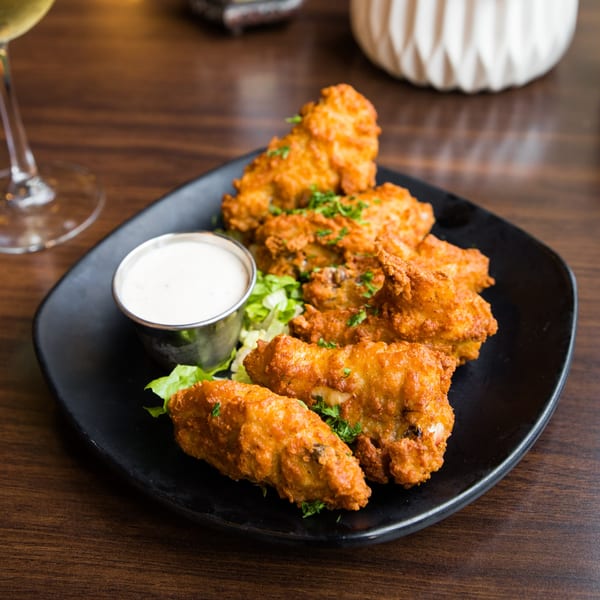Crispy fried chicken tenders with a side of white dipping sauce and lettuce on a black plate.