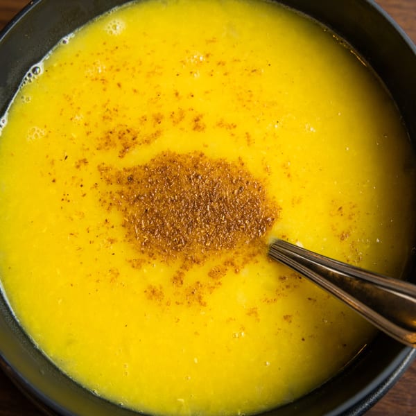 Close-up of a yellow lentil soup with a spoon, garnished with spices.