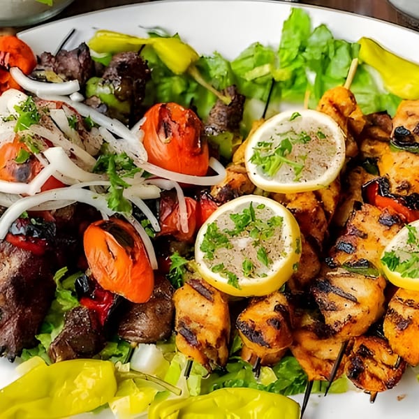 Grilled chicken and beef kabobs with tomatoes, onions, lemons, and lettuce on a white plate.