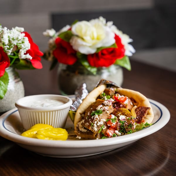 A Kabob House gyro with tzatziki and pickled peppers, with floral decor in the background.