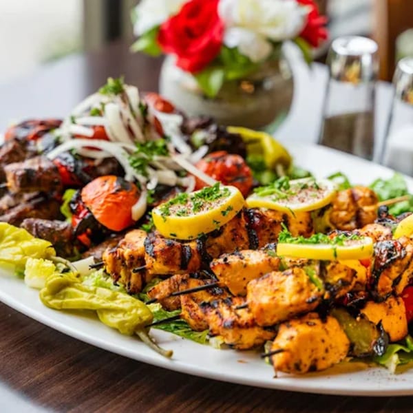 A large platter of grilled chicken and beef kabobs, with vegetables and lemon slices.